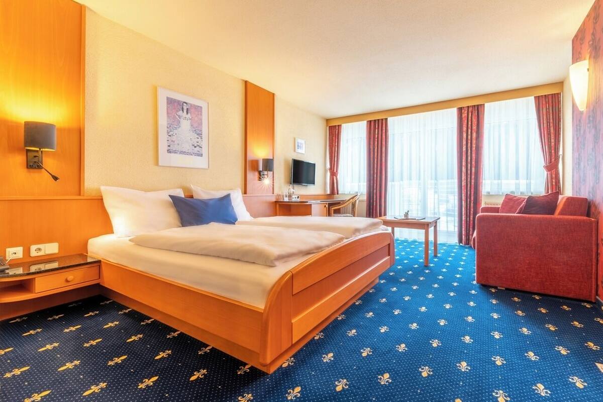 Quarto de hotel com cama, escrivaninha, cadeira, televisão e janela com cortinas.