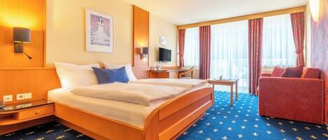 A hotel room with a bed, a desk, a chair, a TV, and a window with curtains.