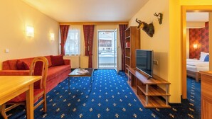 Een hotelkamer met een rode bank, een houten salontafel, een televisie op een houten standaard en een boekenkast.