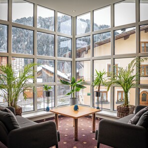 A room with a large window overlooking a snowy mountain landscape, featuring a table with chairs and potted plants. - Hotel Tia Monte Nauders (Nauders)