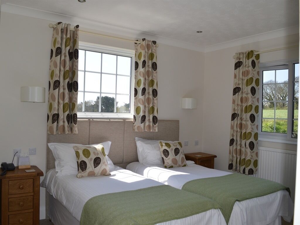 A double room with two beds, a window with curtains, bedside lamps, and a view of greenery outside.