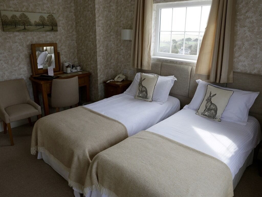 A hotel room with two beds, a desk, a chair, a mirror, and a window with curtains.