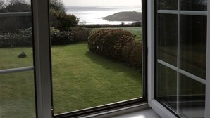 A view from a window overlooking a grassy yard with a body of water and hills in the distance. - Trelawne Hotel (Falmouth)