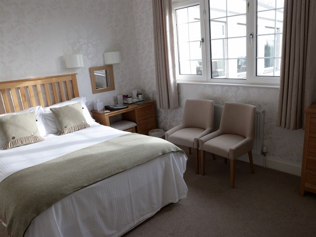 A bedroom with a bed, bedside table, lamp, chair, and a window with curtains.