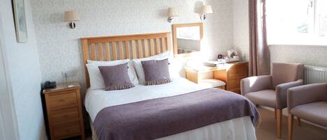 A hotel room with a bed, bedside tables, a desk, a chair, and a window with curtains.