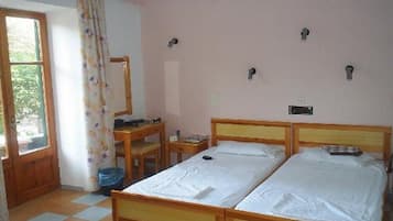 A room with two single beds, a wooden desk, a chair, and a window with a curtain.