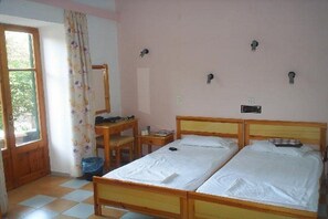 Habitació amb dos llits individuals, un escriptori de fusta, una cadira i una finestra amb cortina.