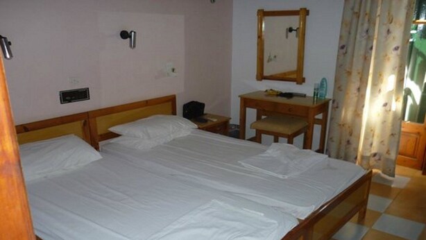 A room with a large bed, a wooden desk, a mirror, and a small table. - Amfitriti (Lesvos)