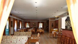 A spacious dining area with high tables and chairs, a long sofa, and a bar area with stools. - Amfitriti (Lesvos)