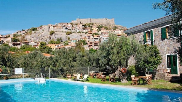 A swimming pool with lounge chairs and a stone building with green shutters. - Amfitriti (Lesvos)
