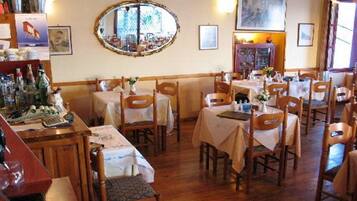 A dining area with round tables and chairs, a mirror on the wall, and a cabinet with bottles.