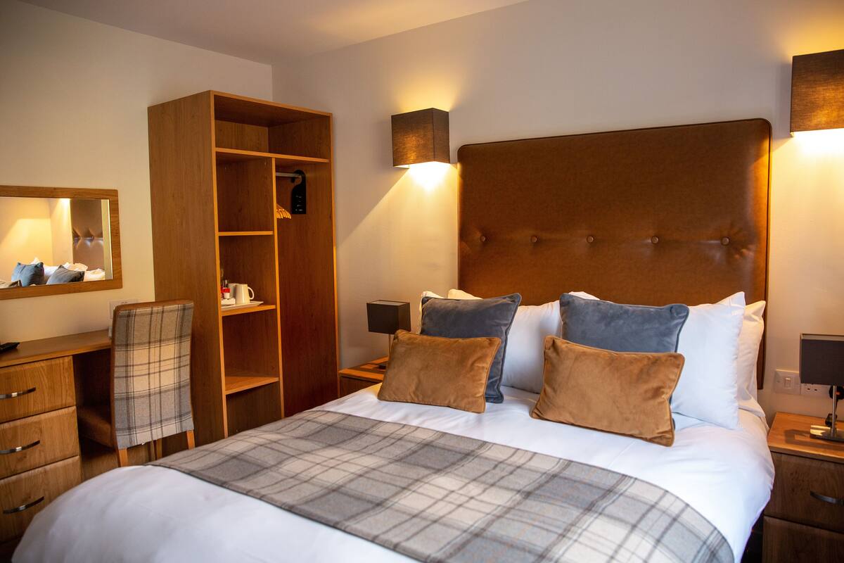 Habitación de hotel ordenada con una cama grande, un armario, un escritorio y una silla.