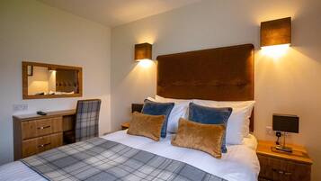 A bedroom with a large bed, two bedside tables, a wooden dresser, a mirror, and wall-mounted lights.