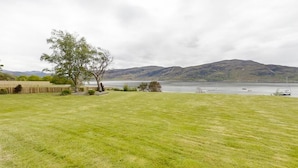 A grassy field with a tree and a lake with boats in the distance and hills in the background. - Harbour House Bed & Breakfast (Ullapool)