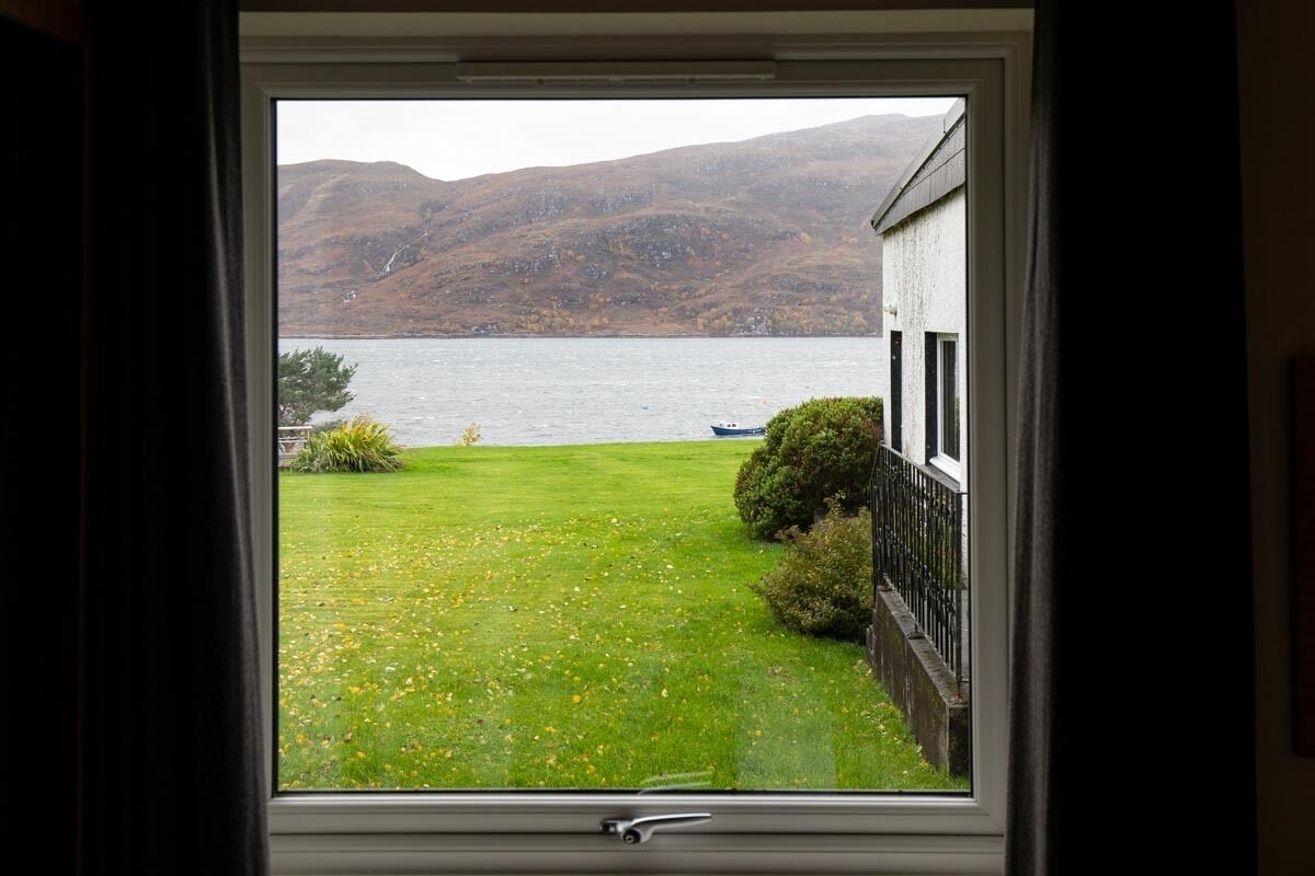 A window view of a grassy area with a lake and hills in the background.