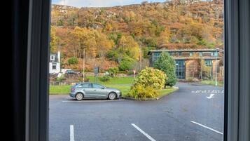 Un parking avec une voiture, un bâtiment et une colline aux couleurs automnales.