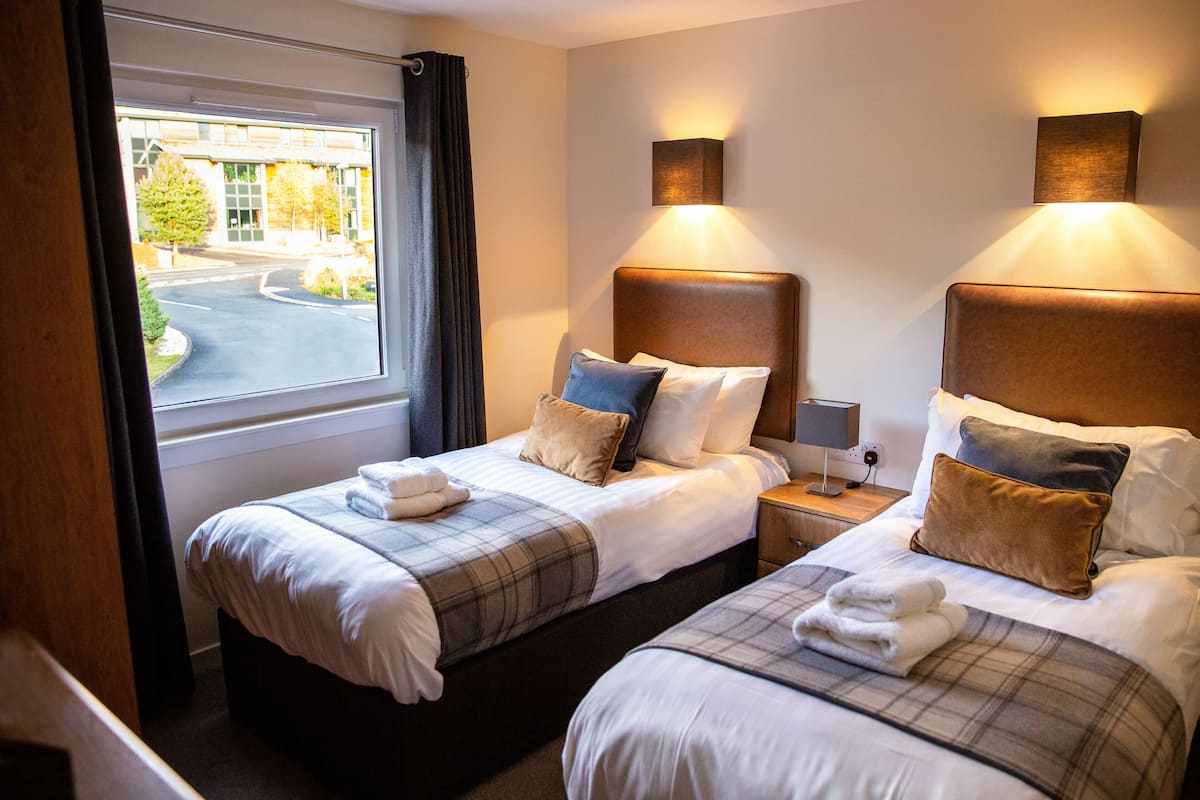 Una habitación de hotel con dos camas, una ventana con cortinas y lámparas fijadas a la pared.