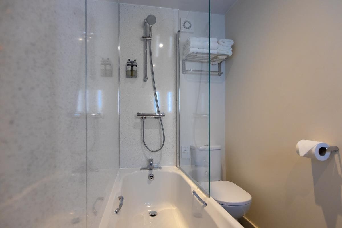 A modern bathroom with a glass-enclosed shower, a white bathtub, and a toilet.