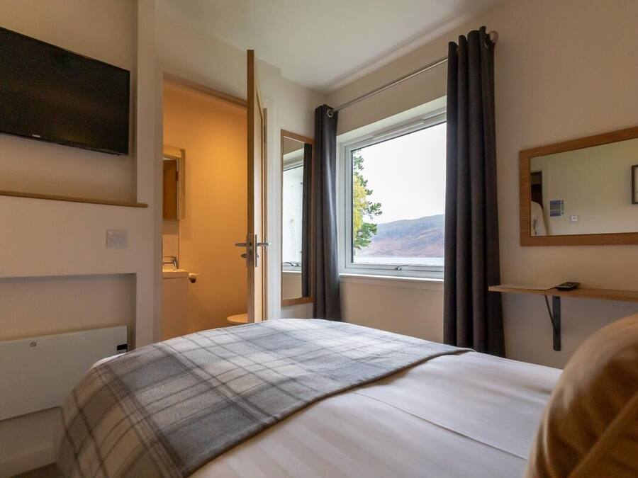 Una habitación de hotel con una cama, un televisor montado en la pared, una ventana con cortinas y un espejo en la pared.
