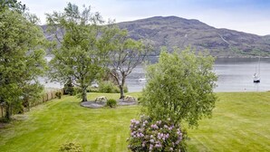 A well-maintained lawn with picnic tables and a bush with pink flowers. - Harbour House Bed & Breakfast (Ullapool)