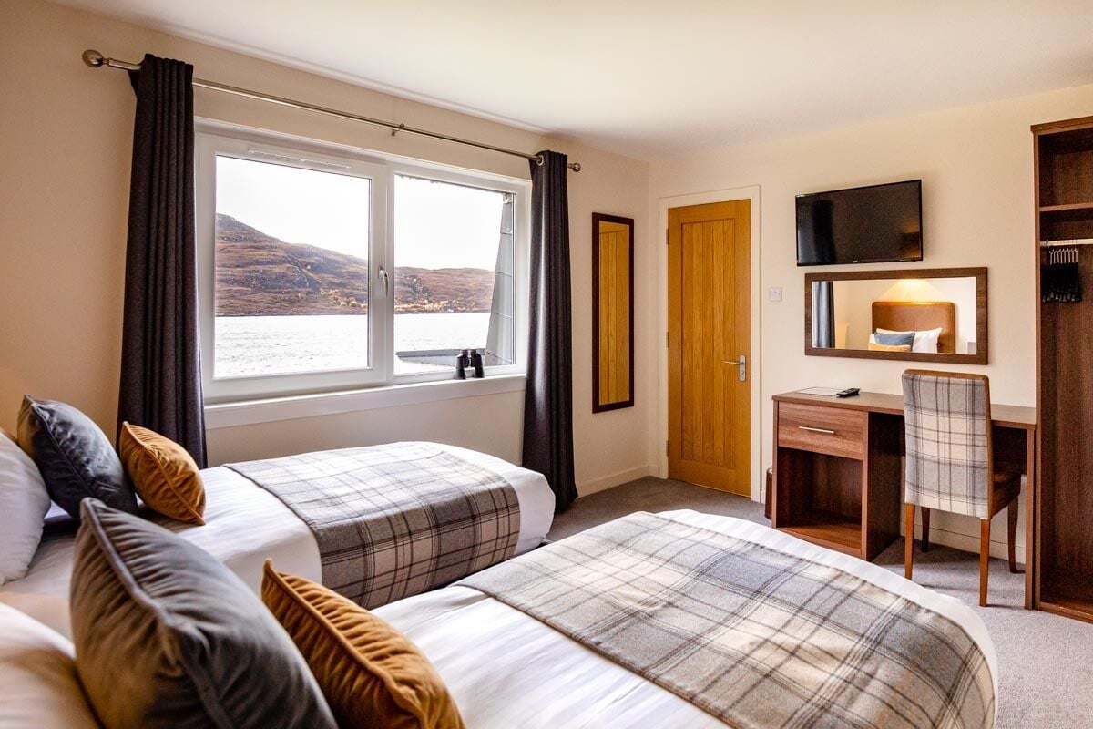 Ein Hotelzimmer mit zwei Betten, einem Schreibtisch, einem Stuhl, einem Fernseher und Meerblick.