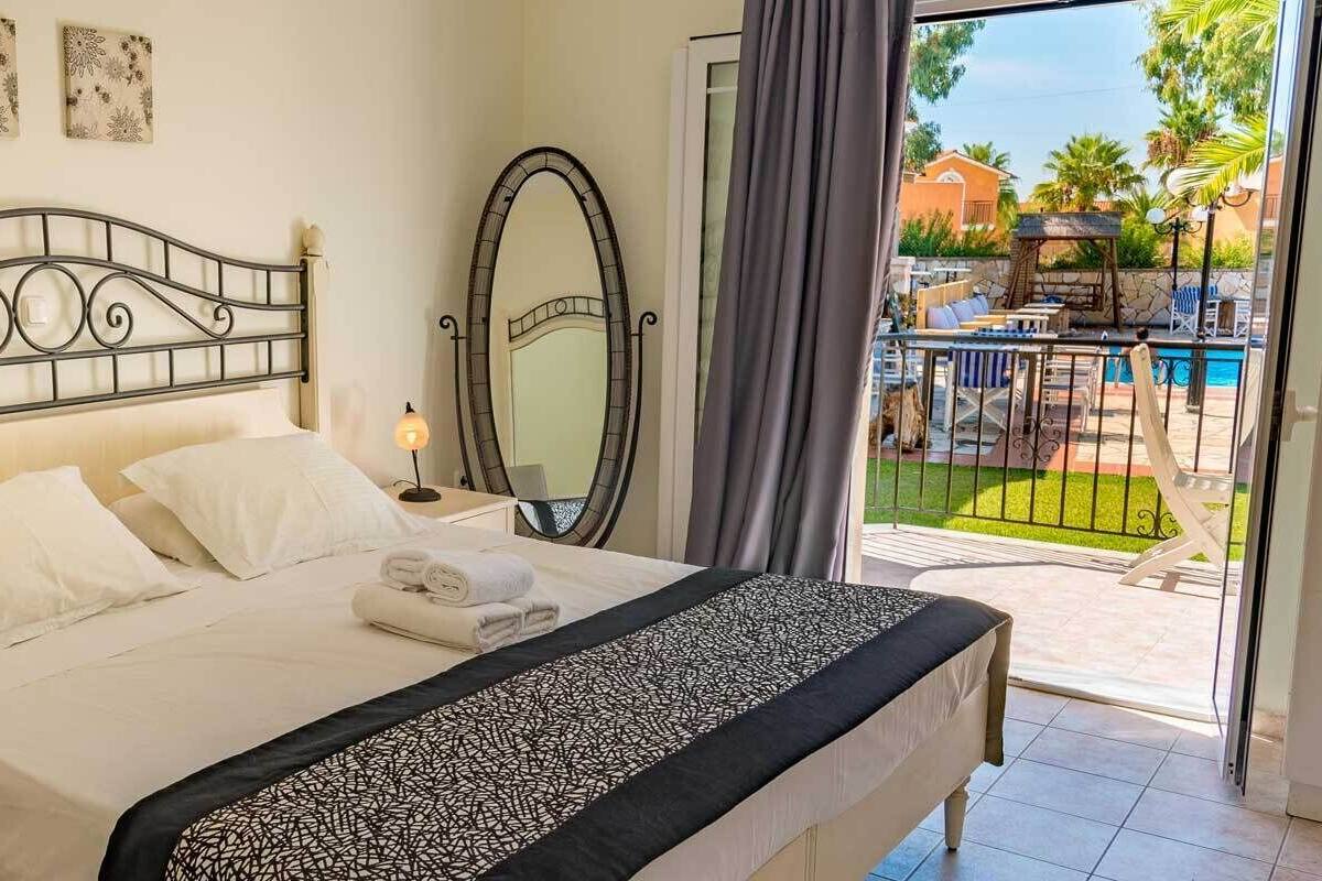 Ein Hotelzimmer mit Bett, Nachttisch, Lampe, Spiegel und Blick auf den Poolbereich.