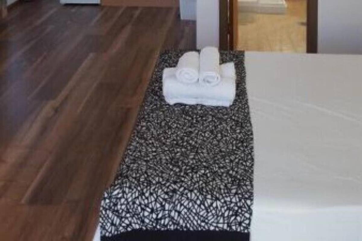 Ein Zimmer mit einem Bett, einem kleinen Tisch mit Handtüchern, Holzboden und einer Küchenzeile mit Schränken und einem Kühlschrank.