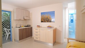 A compact kitchen with wooden cabinets, a sink, and a countertop with fruit bowls. - Villaggio Le Orchidee (Vieste)