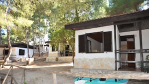 Un bâtiment rustique avec une façade en pierre et des volets en bois, un kayak devant, et des arbres en arrière-plan.