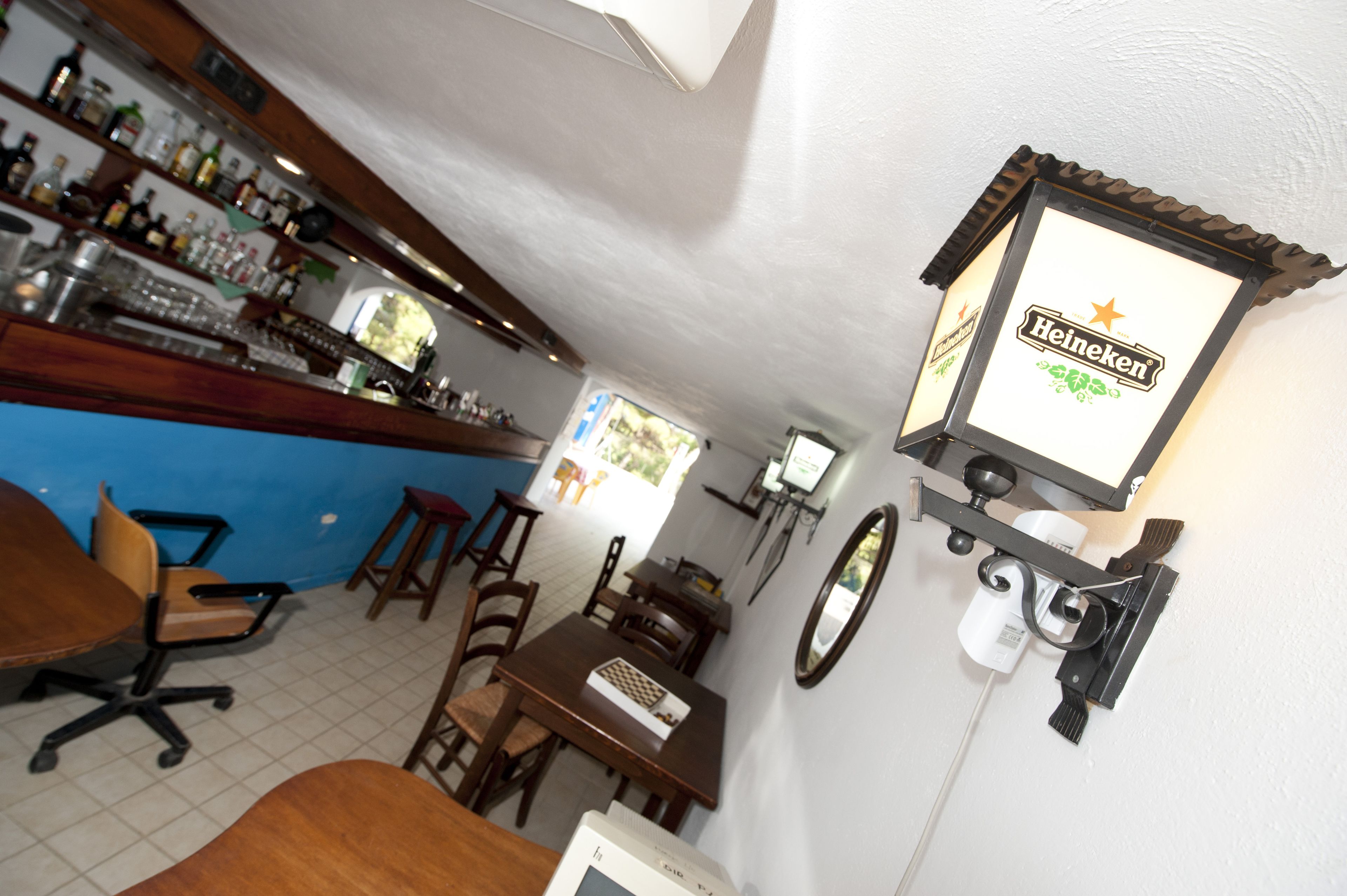Una zona de bar con un letrero de Heineken, mobiliario de madera y suelo de baldosas.