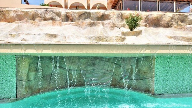 A pool with water cascading down a rocky ledge into a clear pool. - Grand Beach Hotel (Thasos)