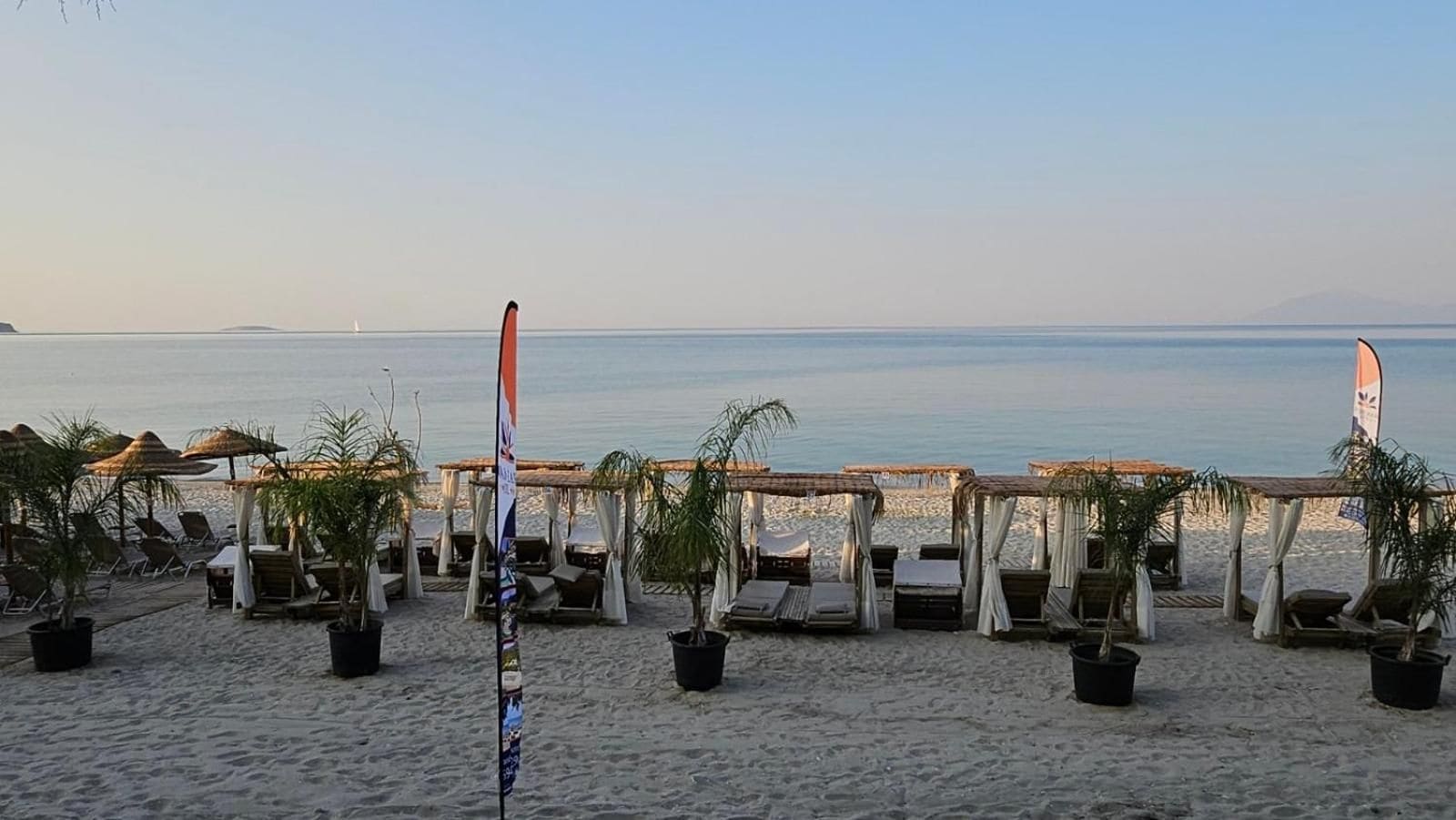 A beachside setting with sun loungers and umbrellas, a flagpole, and a view of the sea.