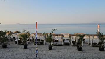A beachside setting with sun loungers and umbrellas, a flagpole, and a view of the sea.