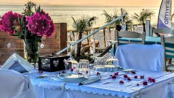 A table set for a meal with a view of the sea, a flag, and a wooden fence.