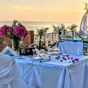 A table set for a meal with a view of the sea, a flag, and a wooden fence. - Grand Beach Hotel (Thasos)