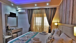 A hotel room with a bed, a desk, a chair, a television, and a window with curtains. - Grand Beach Hotel (Thasos)