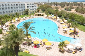 A large outdoor swimming pool surrounded by palm trees and sun loungers, with a building in the background. - Sidi Mansour Resort & Spa (Djerba Midun)