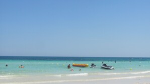 A beach with clear water, a sandy shore, and a few people and watercraft.