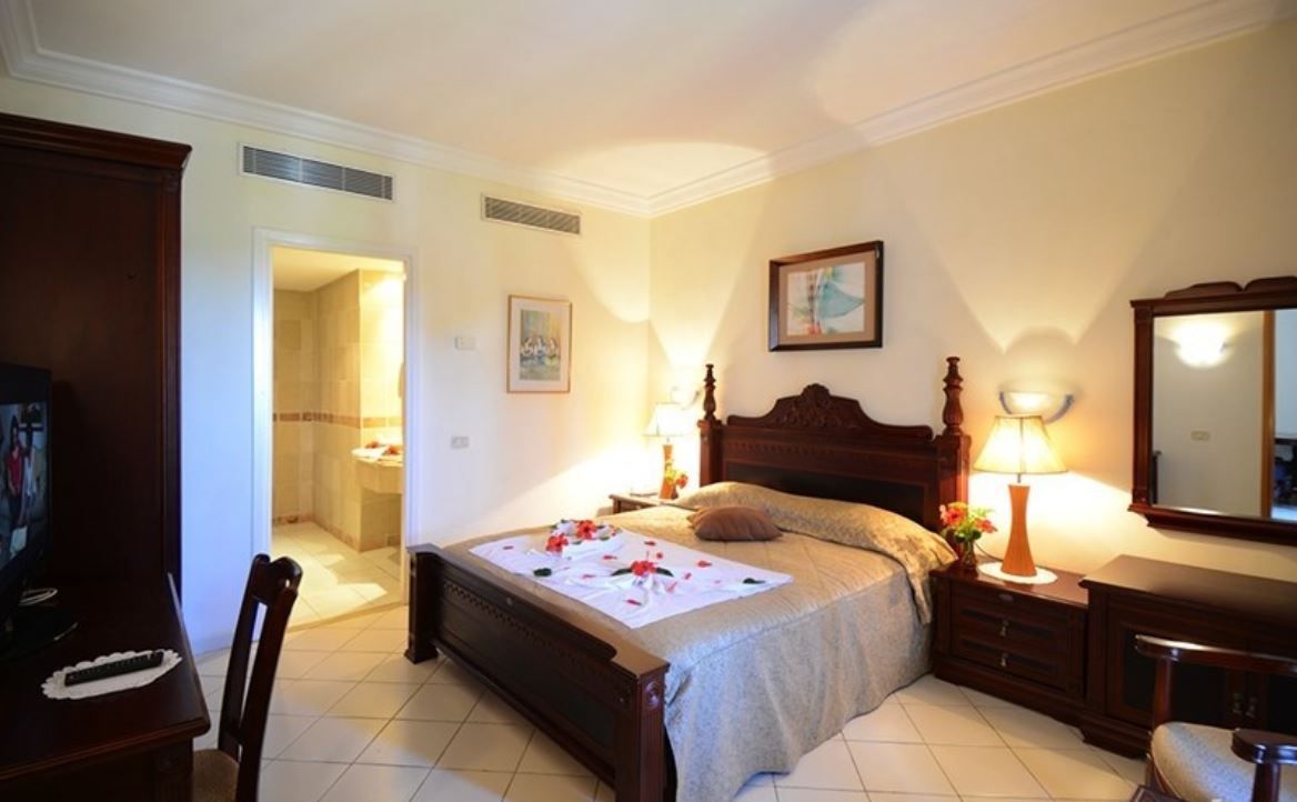 Un dormitorio con una cama de madera, lámparas de noche, un espejo y una mesita con lámpara.