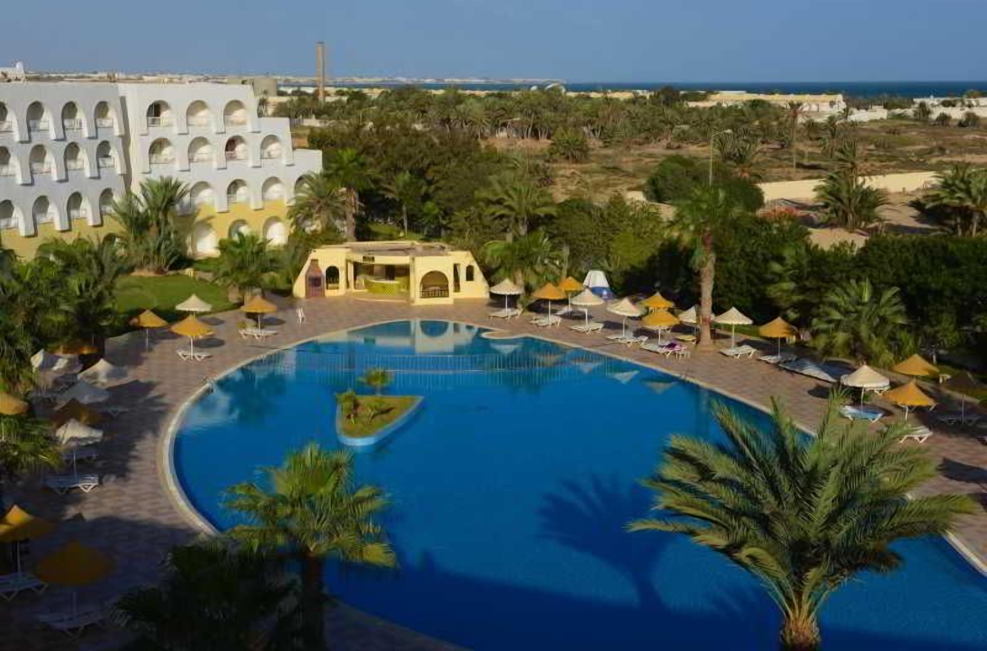 Un resort con una gran piscina, palmeras y vistas al mar.