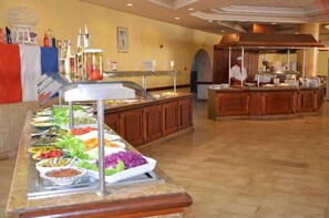 A buffet with various food options, a kitchen area, and a counter with a staff member. - Sidi Mansour Resort & Spa (Djerba Midun)
