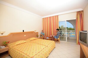A hotel room with a bed, a TV, a small table, and a balcony with a pool view. - Sidi Mansour Resort & Spa (Djerba Midun)