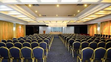 Un salón de conferencias con filas de sillas, un escenario e iluminación empotrada en el techo.
