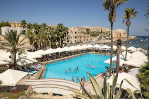 A swimming pool with lounge chairs and umbrellas, surrounded by palm trees and buildings. - Beach Garden Hotel (St. Julian's)