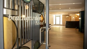 Ein Empfangsbereich im modernen Stil, mit einer Glastrennwand mit dem Schriftzug „beachgarden hotel“ und einem Empfangsschalter.
