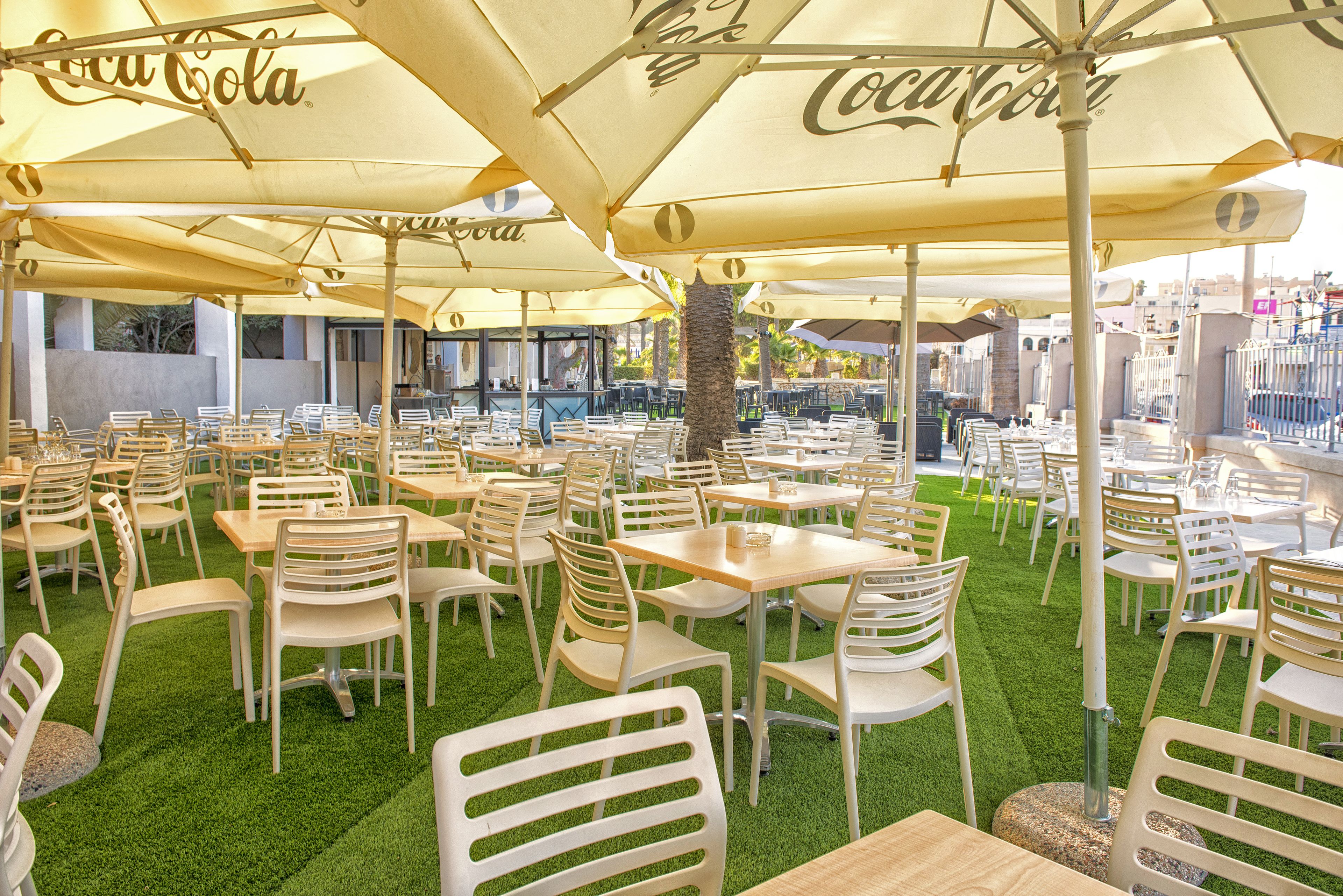 An outdoor dining area with tables and chairs, large umbrellas, and artificial grass.