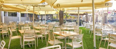 An outdoor dining area with tables and chairs, large umbrellas, and artificial grass.