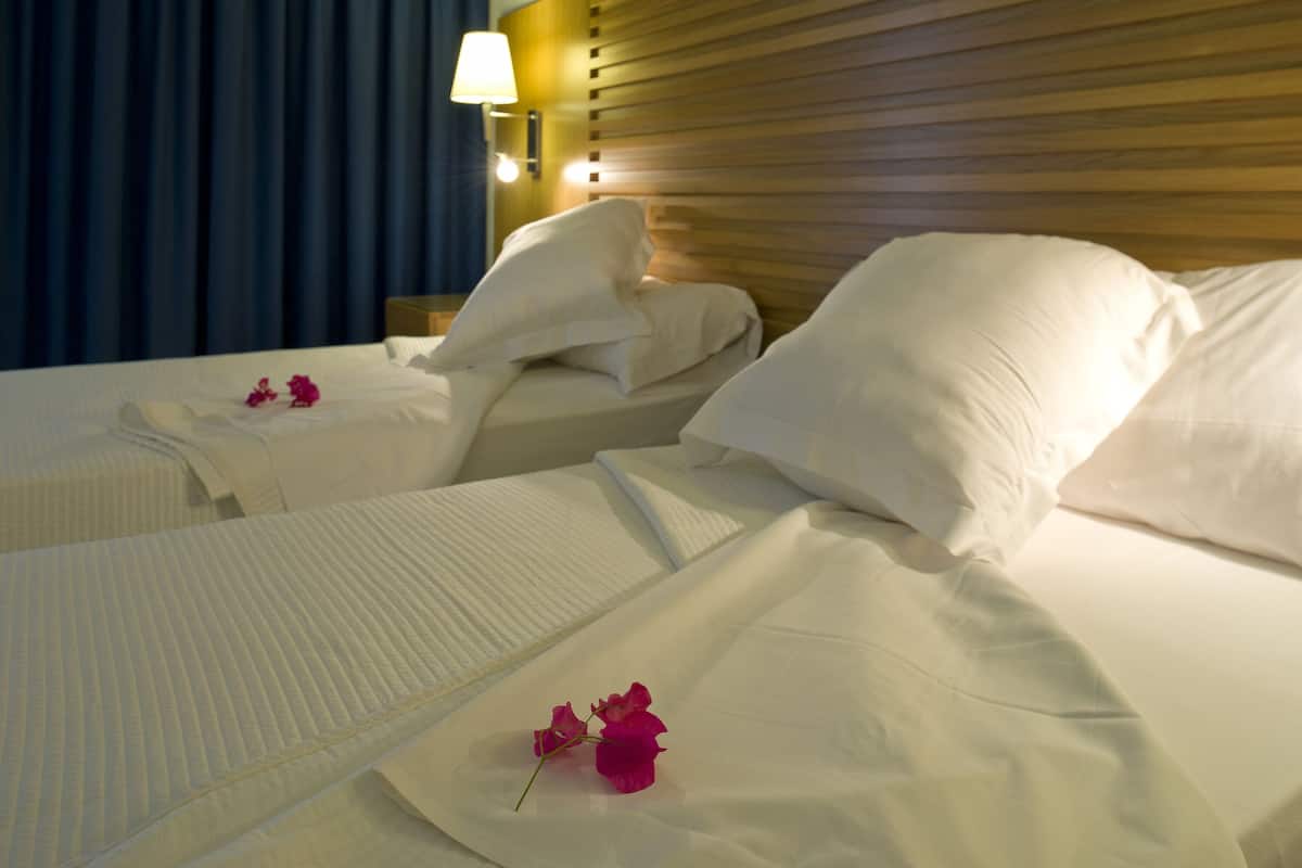 A hotel room with two beds, a wooden headboard, a nightstand with a lamp, and a painting on the wall.