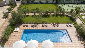 A rooftop pool area with multiple lounge chairs, umbrellas, and a small hot tub.