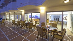 A spacious indoor dining area with multiple tables and chairs, large windows, and a view of the cityscape.